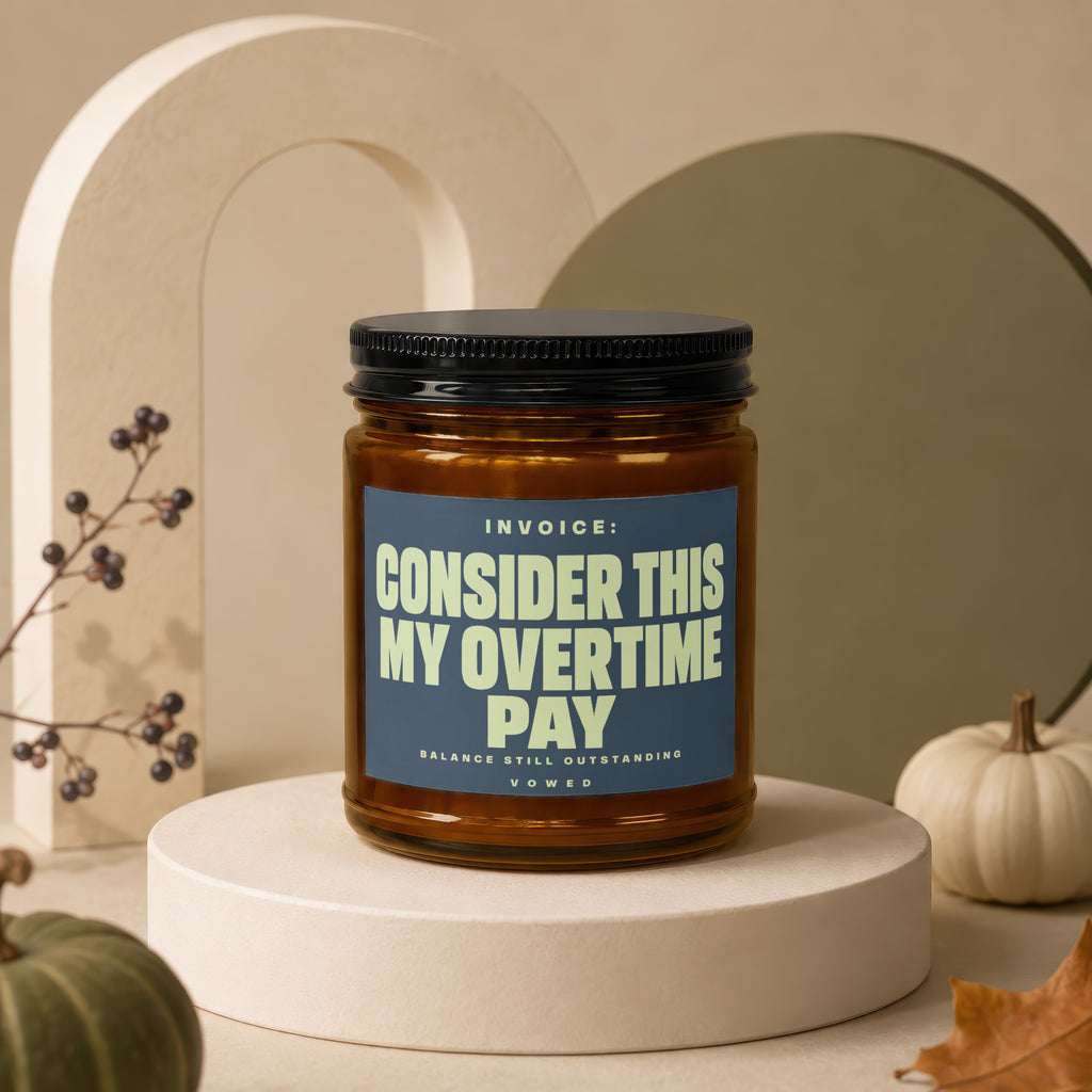 Amber jar candle with blue label reading "INVOICE: CONSIDER THIS MY OVERTIME PAY".