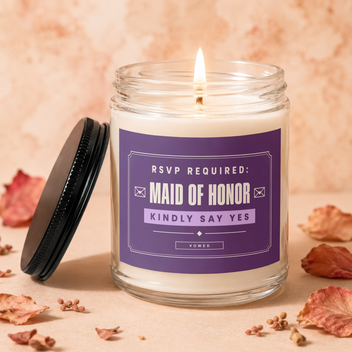 Glass candle with lit wick and purple label saying "Maid of Honor Kindly Say Yes".