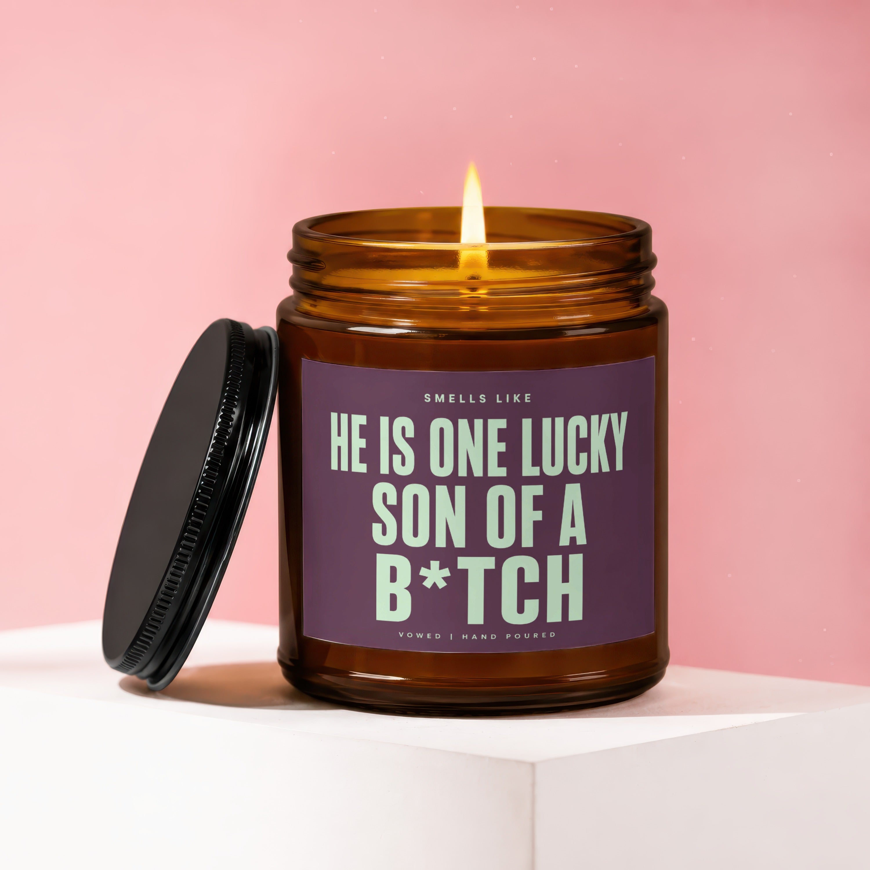 Amber candle with burning wick, reads "He is one lucky son of a b*tch".