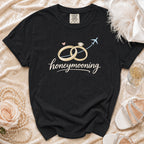 Black t-shirt with "honeymooning" text, wedding rings, airplane, and a rose.
