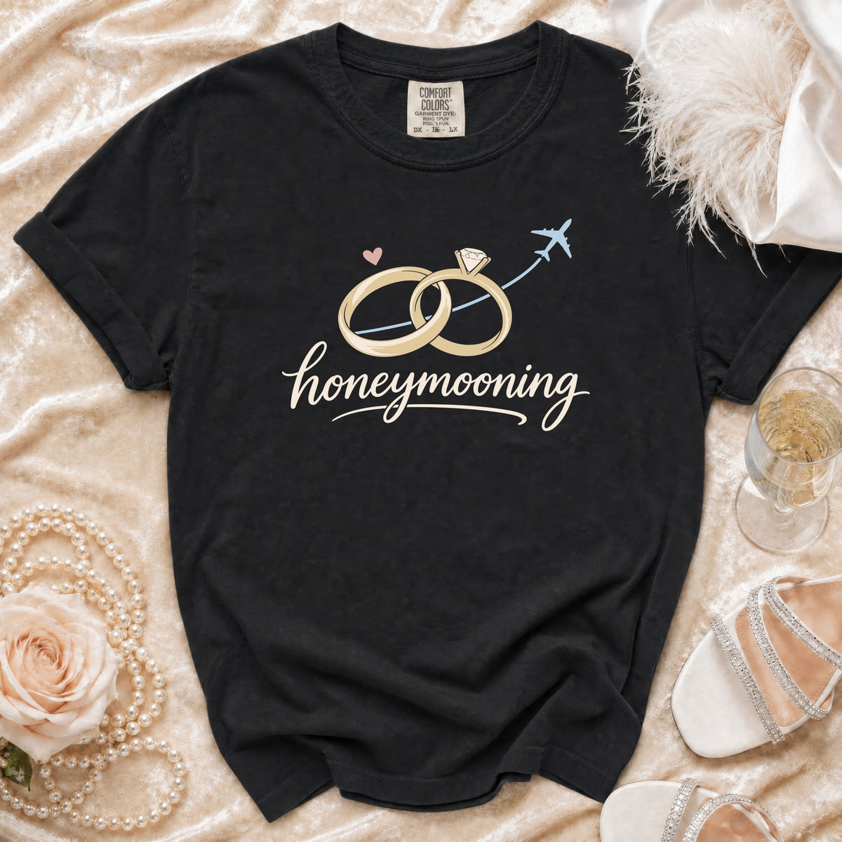 Black t-shirt with "honeymooning" text, wedding rings, airplane, and a rose.