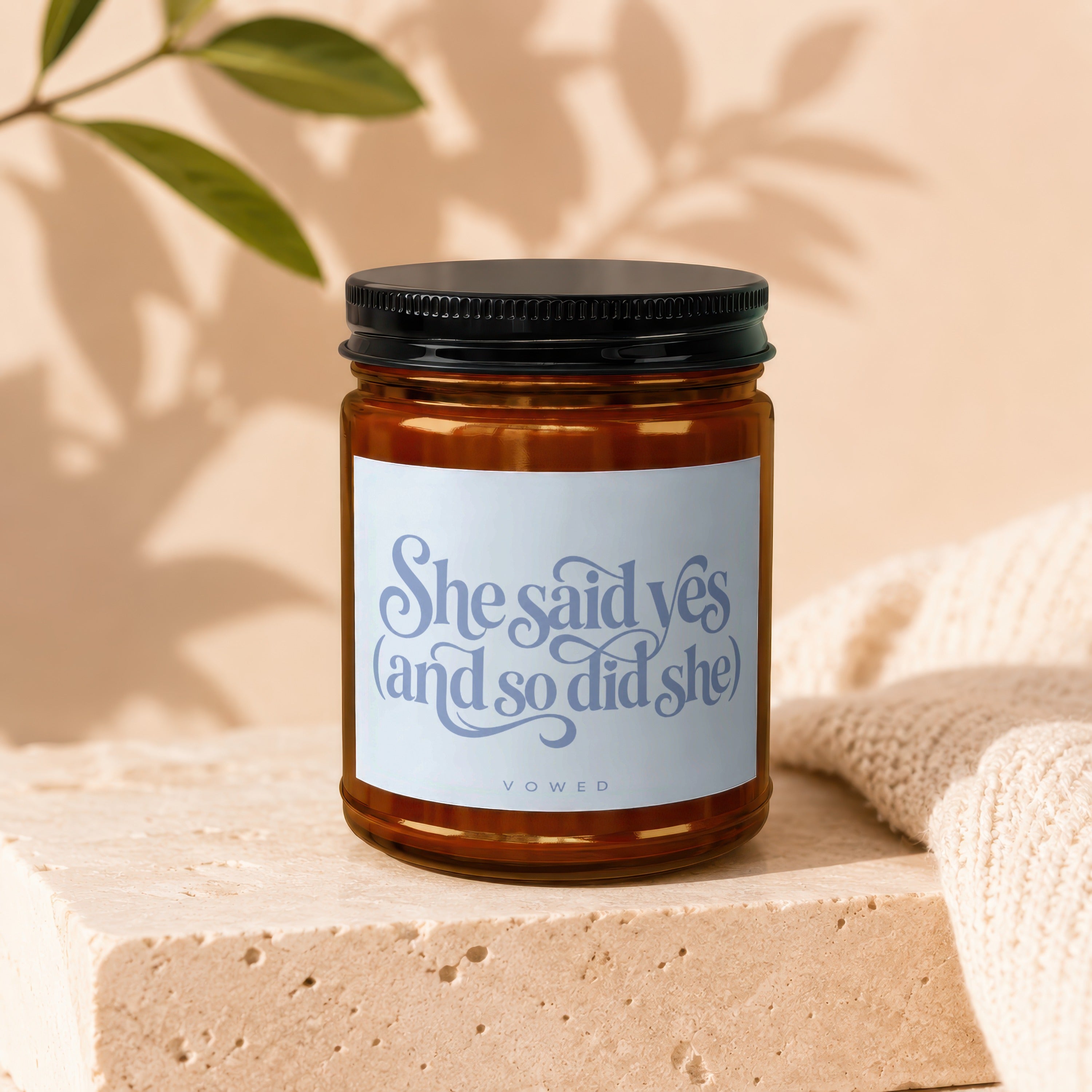 Amber jar candle with black lid, white label reads "She said yes (and so did she) VOWED".