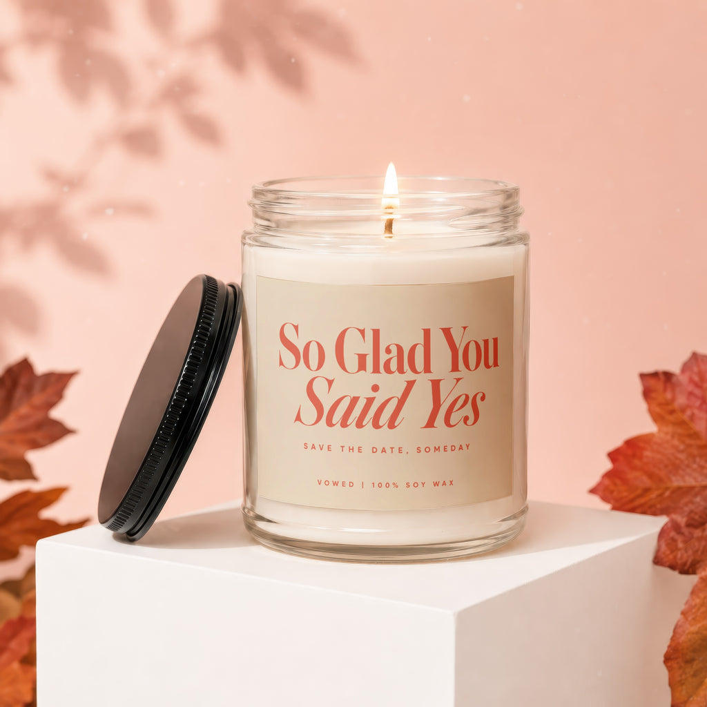 Glass candle with lit wick and "So Glad You Said Yes" text.