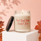 Glass candle with lit wick and "So Glad You Said Yes" text.