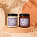Two candles with "Officially Dating Engaged" text on purple labels rest on display pedestals.