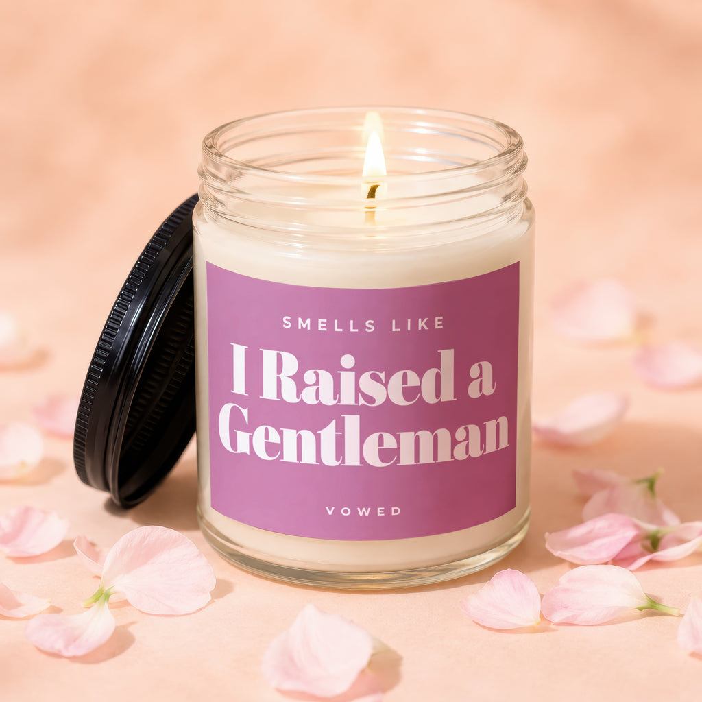 Candle with lit wick and purple label reading "Smells Like I Raised a Gentleman Vowed."