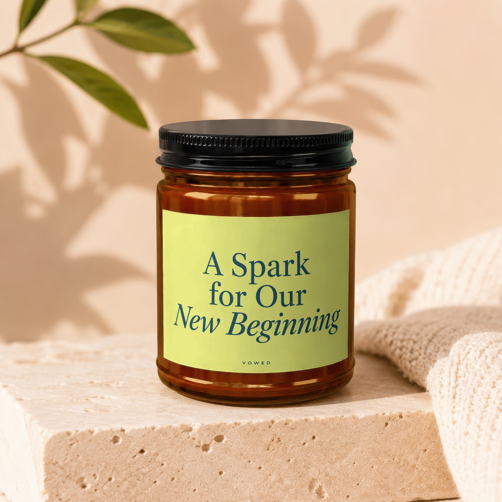 Amber jar candle with black lid, text "A Spark for Our New Beginning" and "vowed".