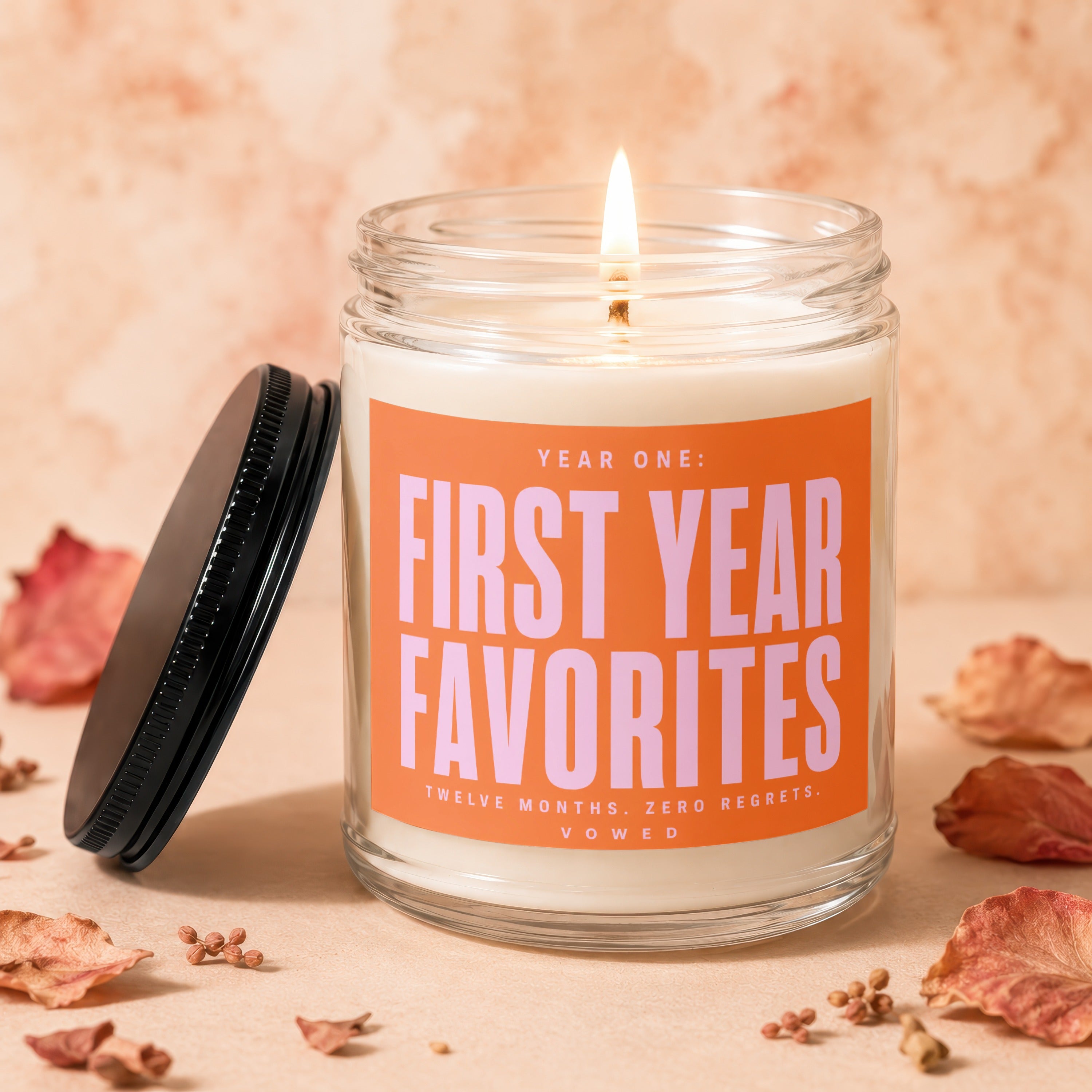Glass jar candle with lit wick and orange label reading "FIRST YEAR FAVORITES".