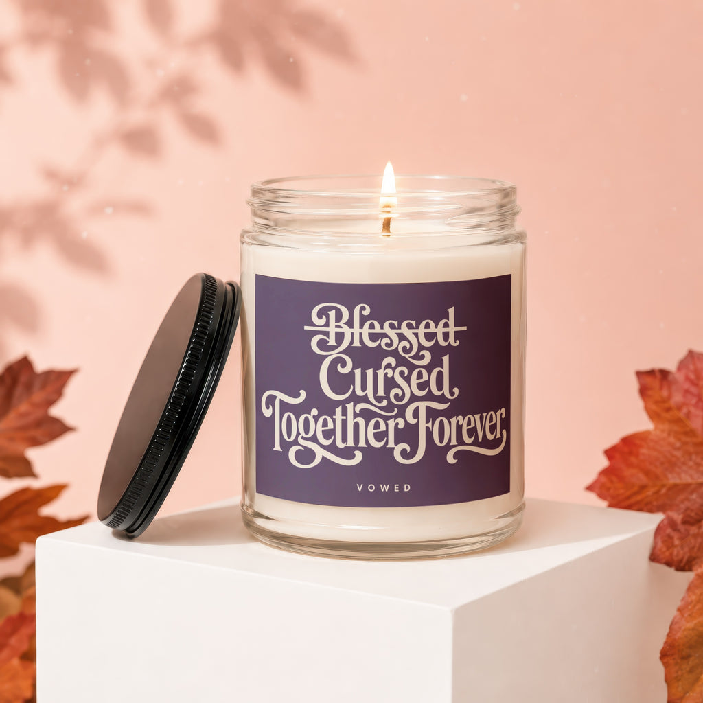Glass jar candle with lit flame and "Blessed Cursed Together Forever" text on label.