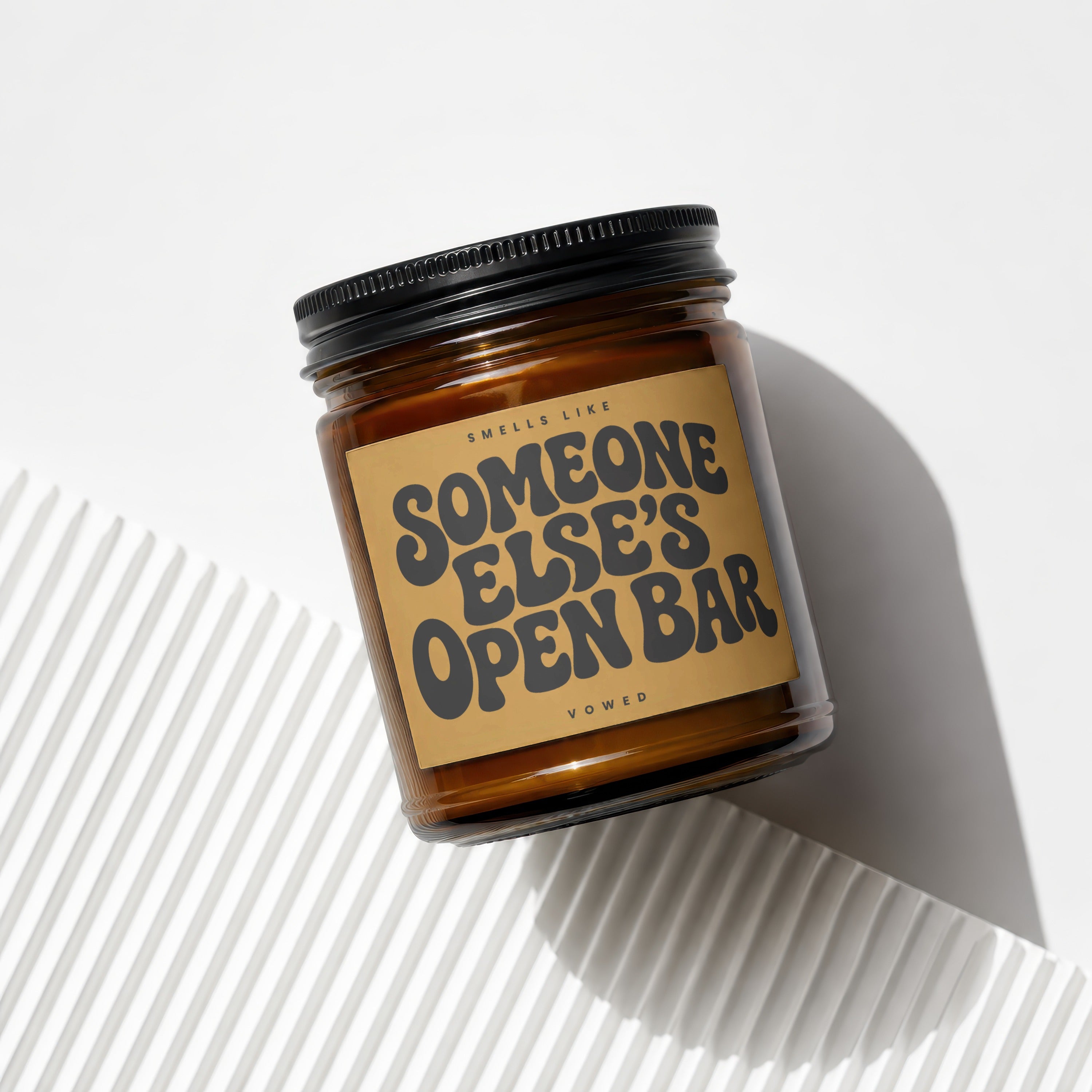 Amber glass candle with black lid reads "Smells like Someone Else's Open Bar".