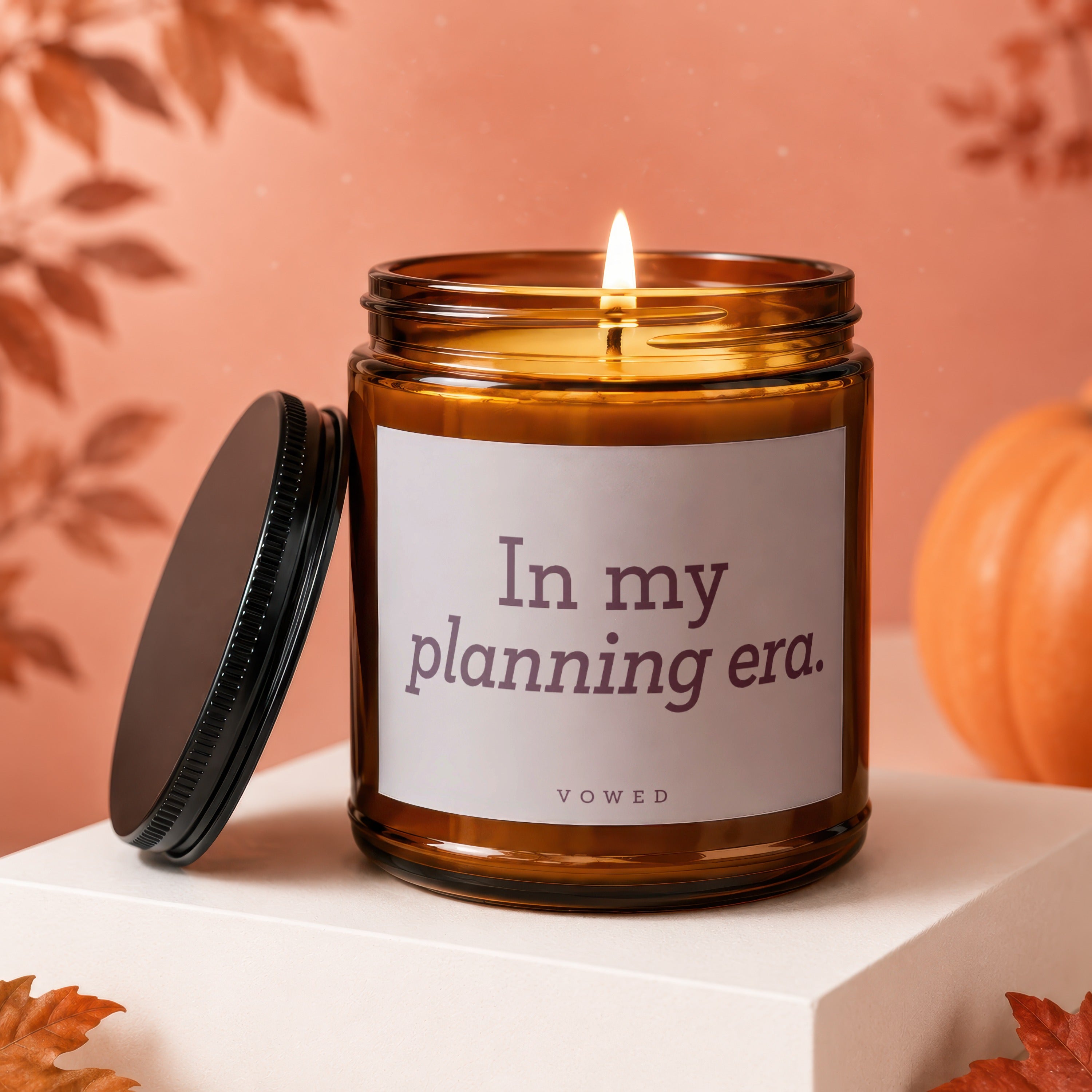 Amber glass candle with a lit flame and label reading "In my planning era. VOCED."