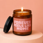 Amber jar candle with lit wick, lid off, labeled "Forever Feels Like Home".