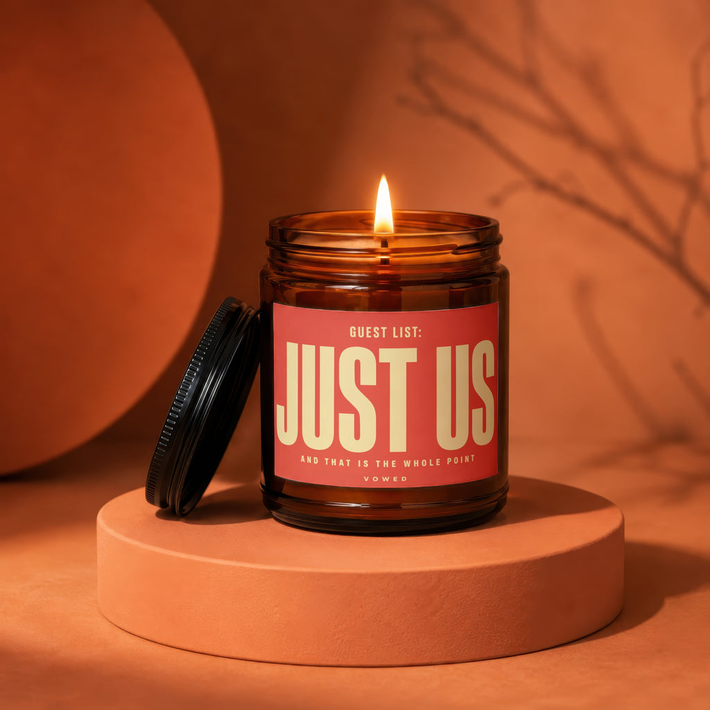 Amber candle with lit wick, label reads "GUEST LIST: JUST US".
