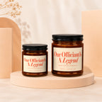 Two amber glass candles with cream labels, reading "Our Officiant Is A Legend."
