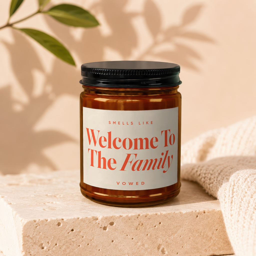 Amber glass candle with black lid labeled "Smells Like Welcome To The Family Vowed".