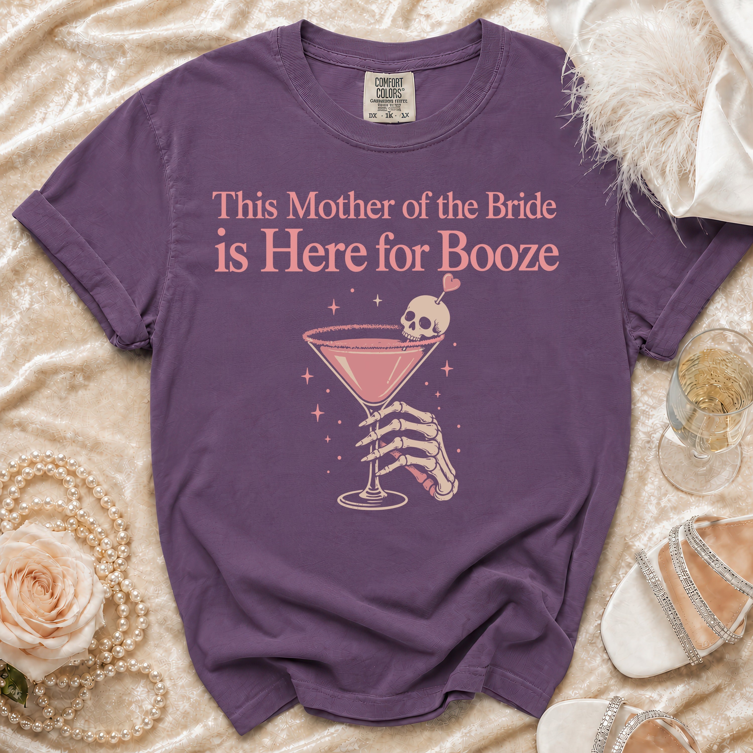 Purple t-shirt with "This Mother of the Bride is Here for Booze" text and skeleton hand holding a cocktail.
