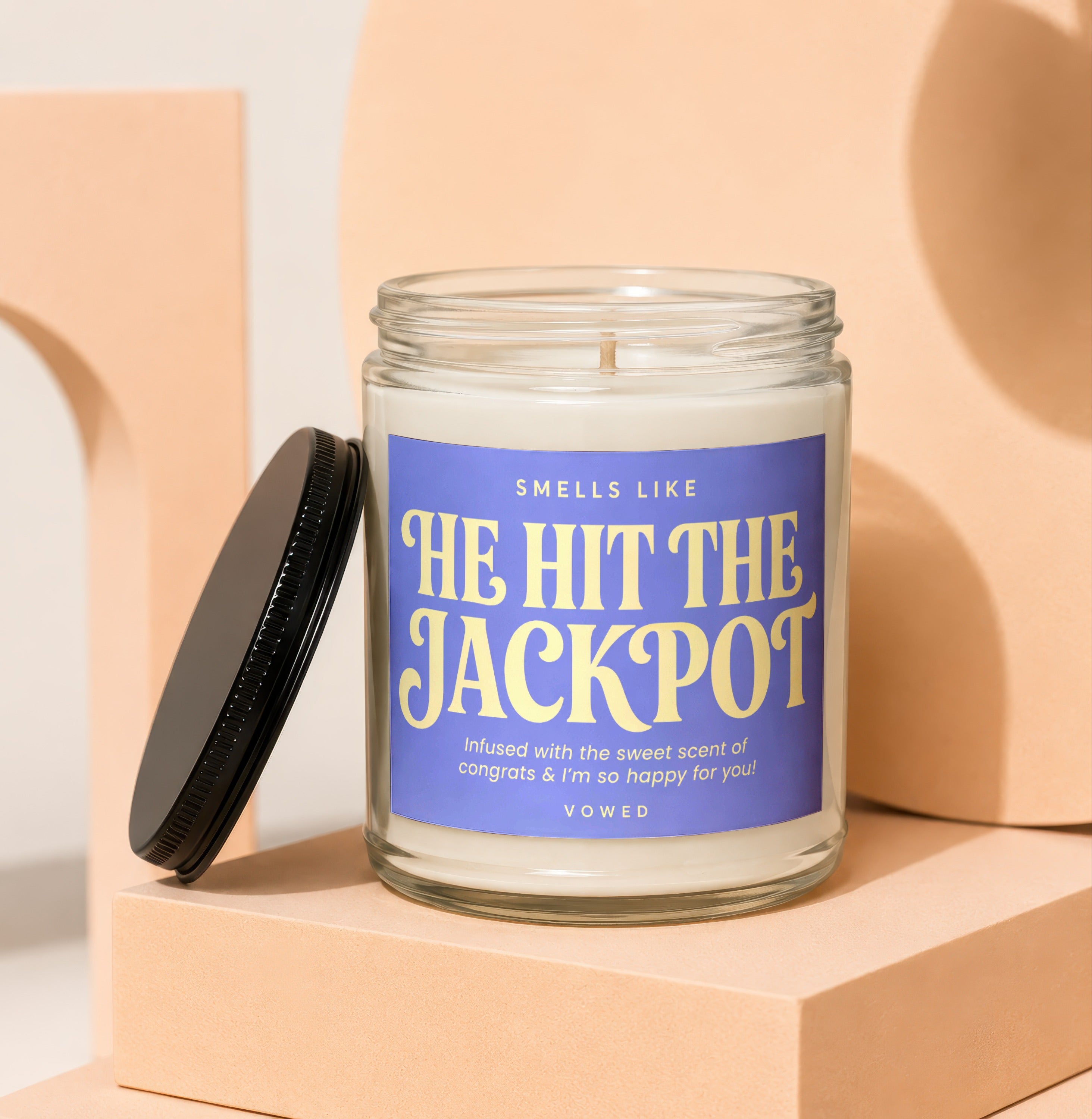 Candle with purple label that says "Smells Like He Hit The Jackpot".