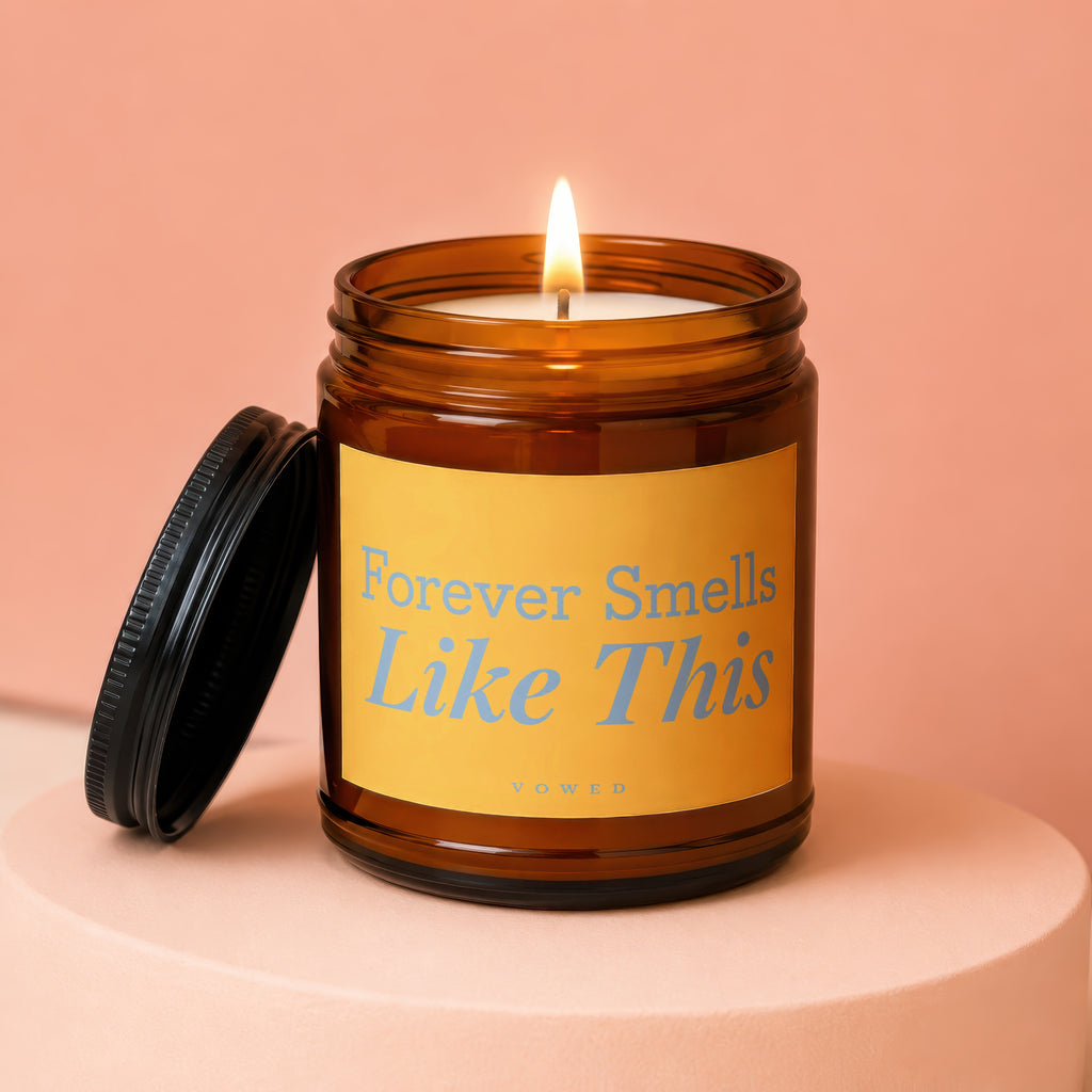 Lit amber glass candle with yellow label and black lid inscribed "Forever Smells Like This"
