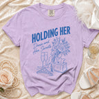 Purple t-shirt with blue graphic text "HOLDING HER Dress and Her Secrets" and illustrations.