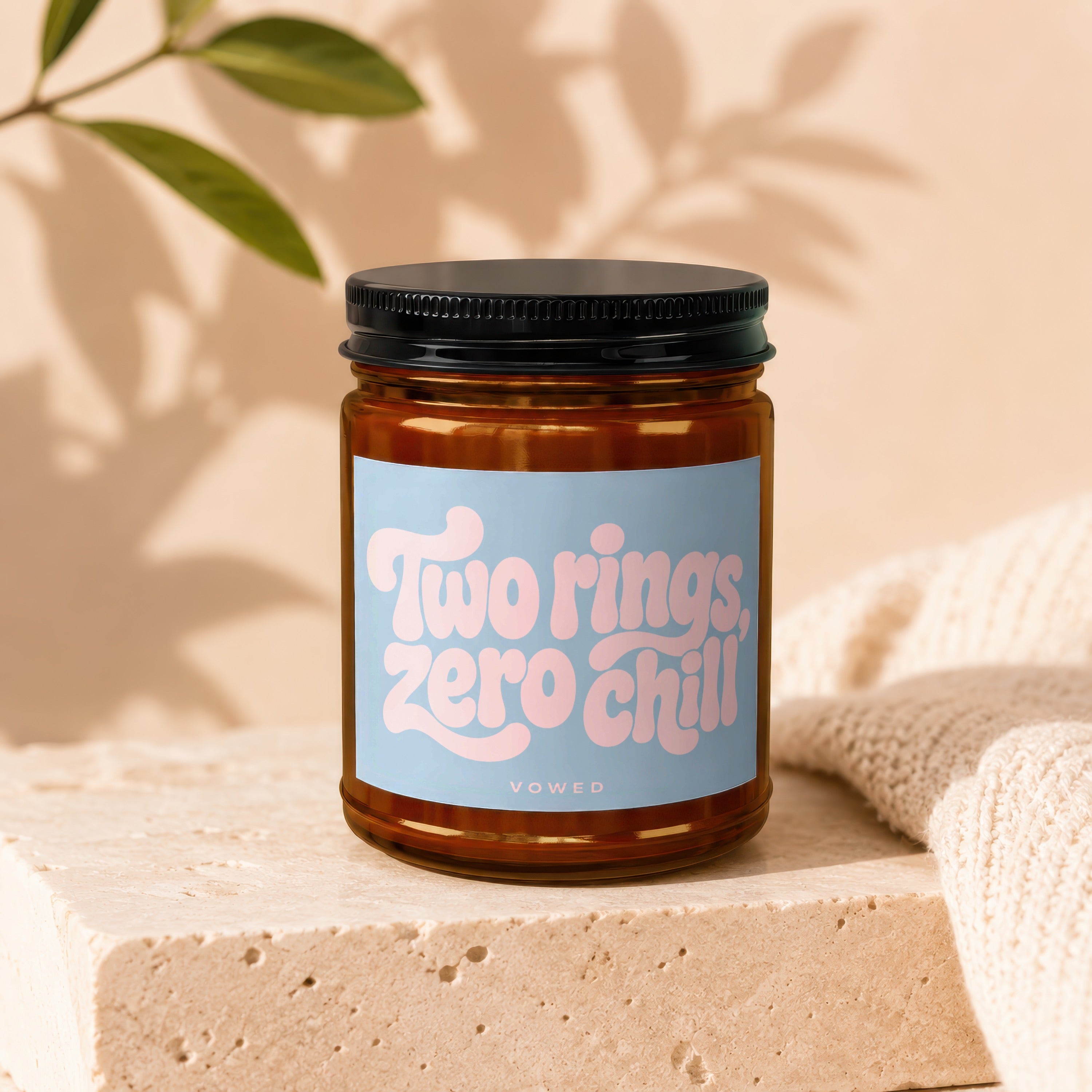 Amber-tinted glass candle with "Two rings, zero chill" text on blue label.