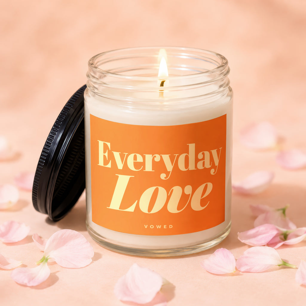 Glass jar candle with orange label that reads "Everyday Love," surrounded by pink petals.