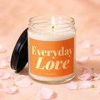 Glass jar candle with orange label that reads "Everyday Love," surrounded by pink petals.