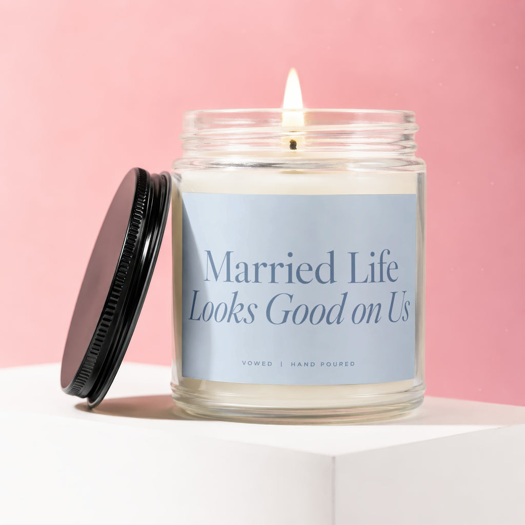 Jar candle with lit flame and black lid, reads "Married Life Looks Good on Us".