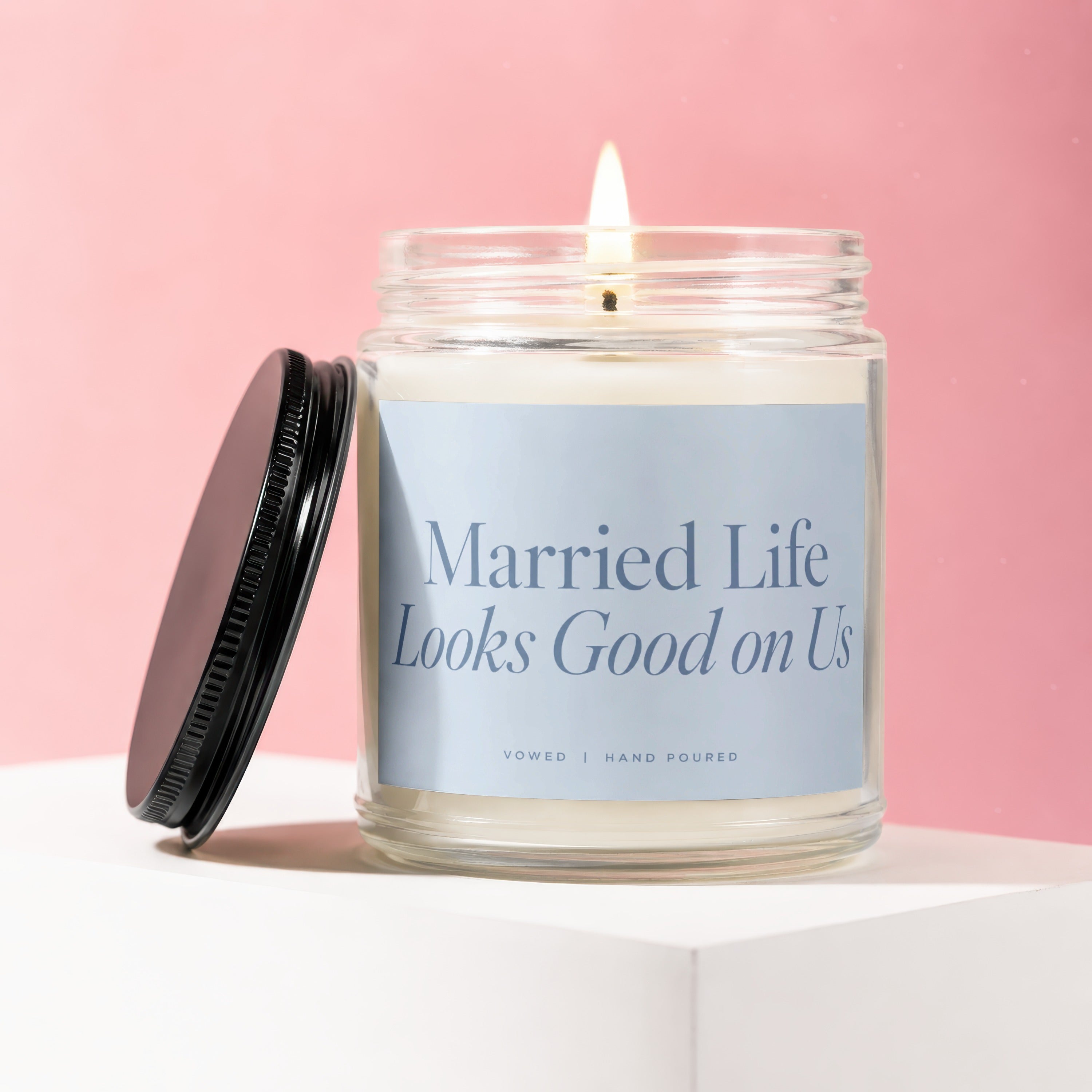 Jar candle with lit flame and black lid, reads "Married Life Looks Good on Us".