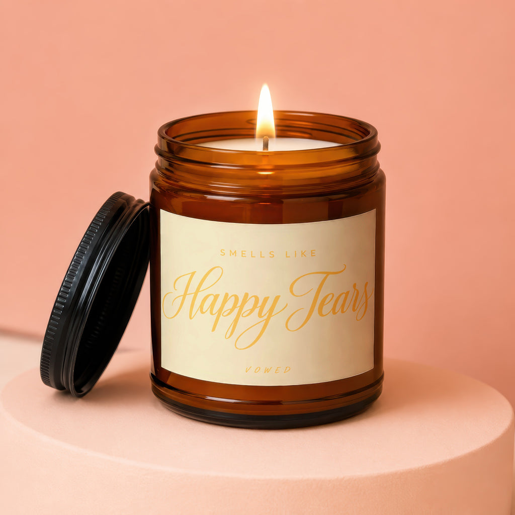 Amber jar candle with lit wick and black lid, featuring "Smells Like Happy Tears" text.