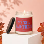 Lit candle in jar with red label that reads "SMELLS LIKE YOU'RE A MAID OF HONOR".