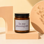 Amber jar candle with black lid displaying "In my planning era." text.