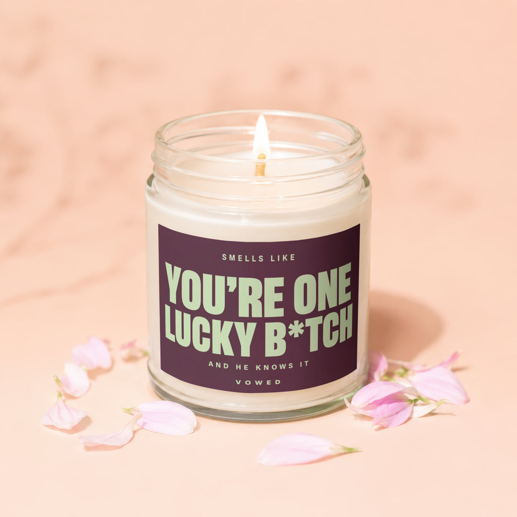 Candle with "You're One Lucky B*tch And He Knows It Vowed" text and pink petals.