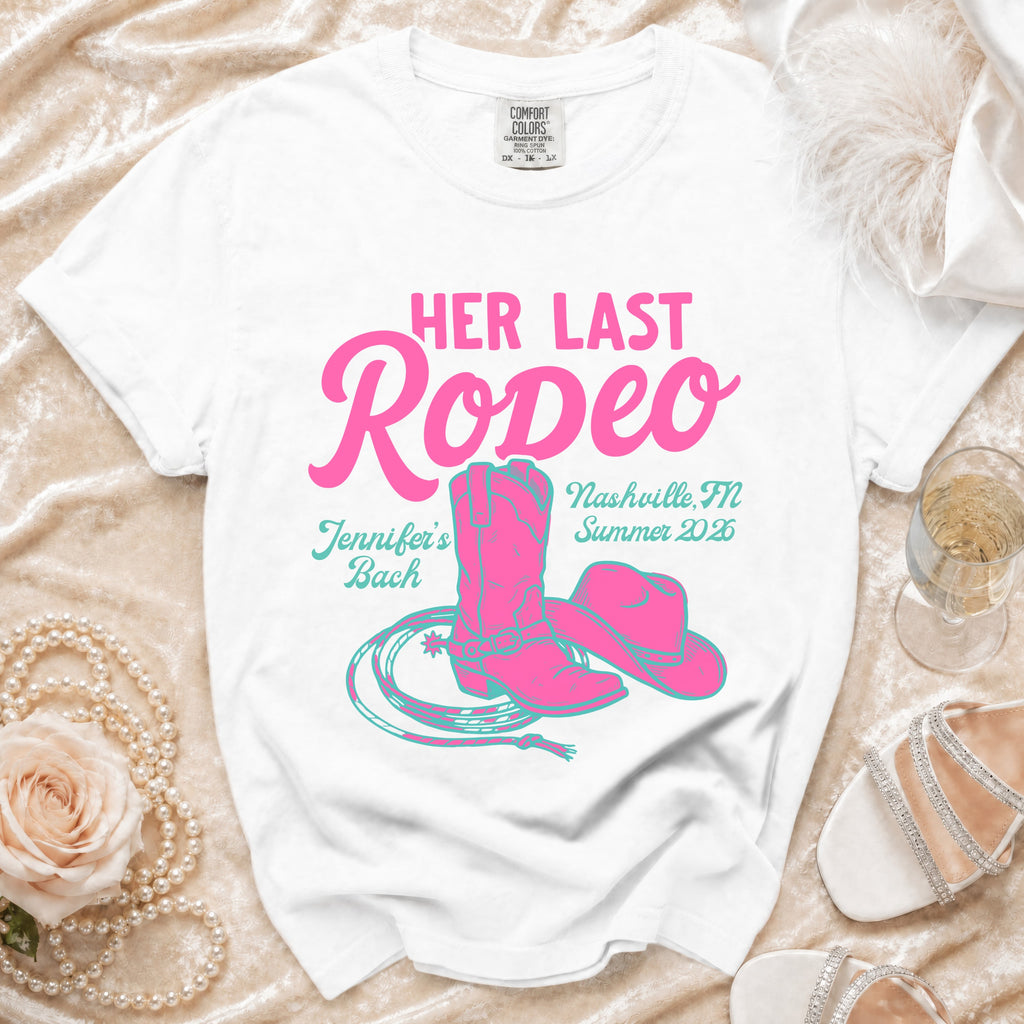 White t-shirt with "Her Last Rodeo" in pink and turquoise, boots, hat, lasso, and text.