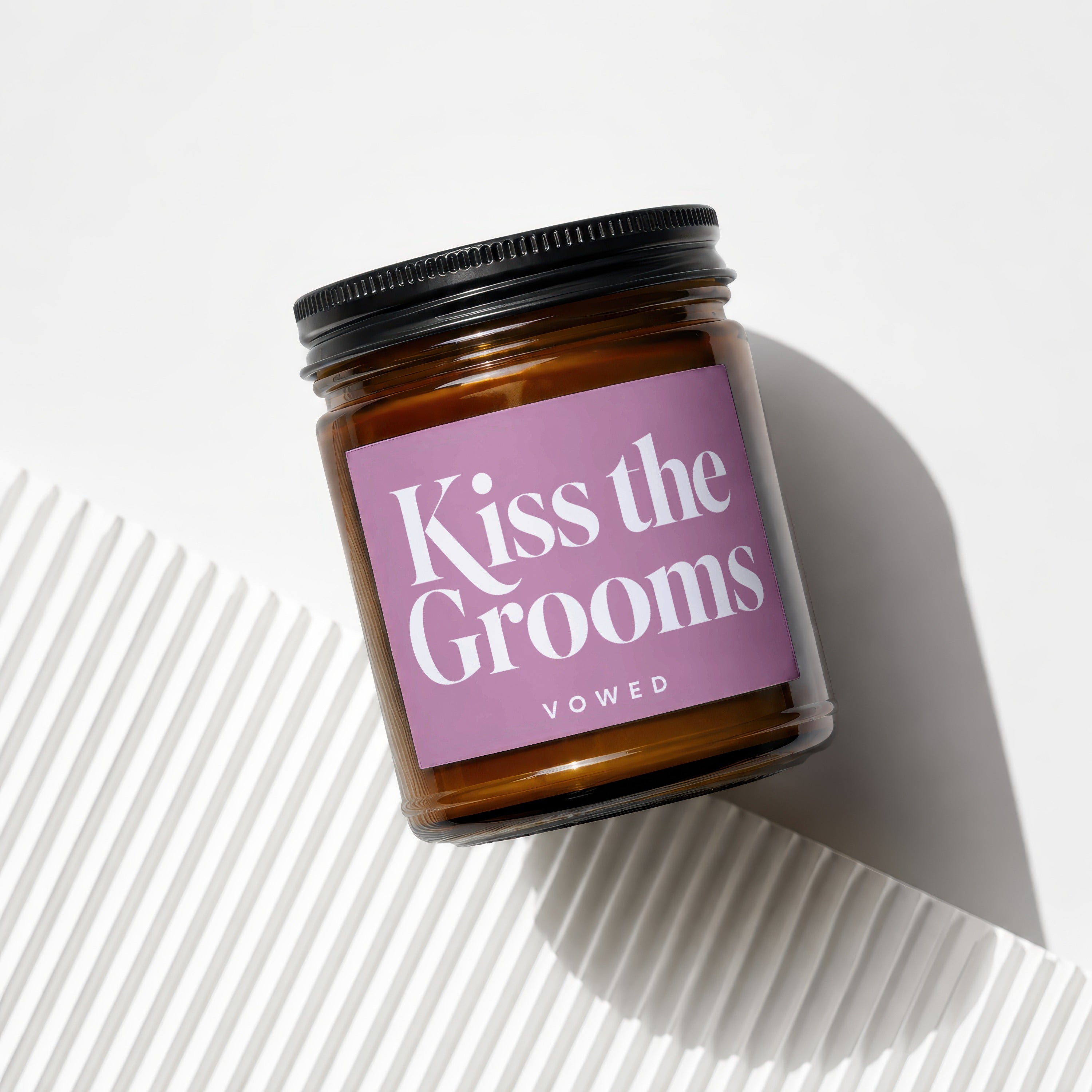Amber jar candle with pink label that reads "Kiss the Grooms" and "VOWED".
