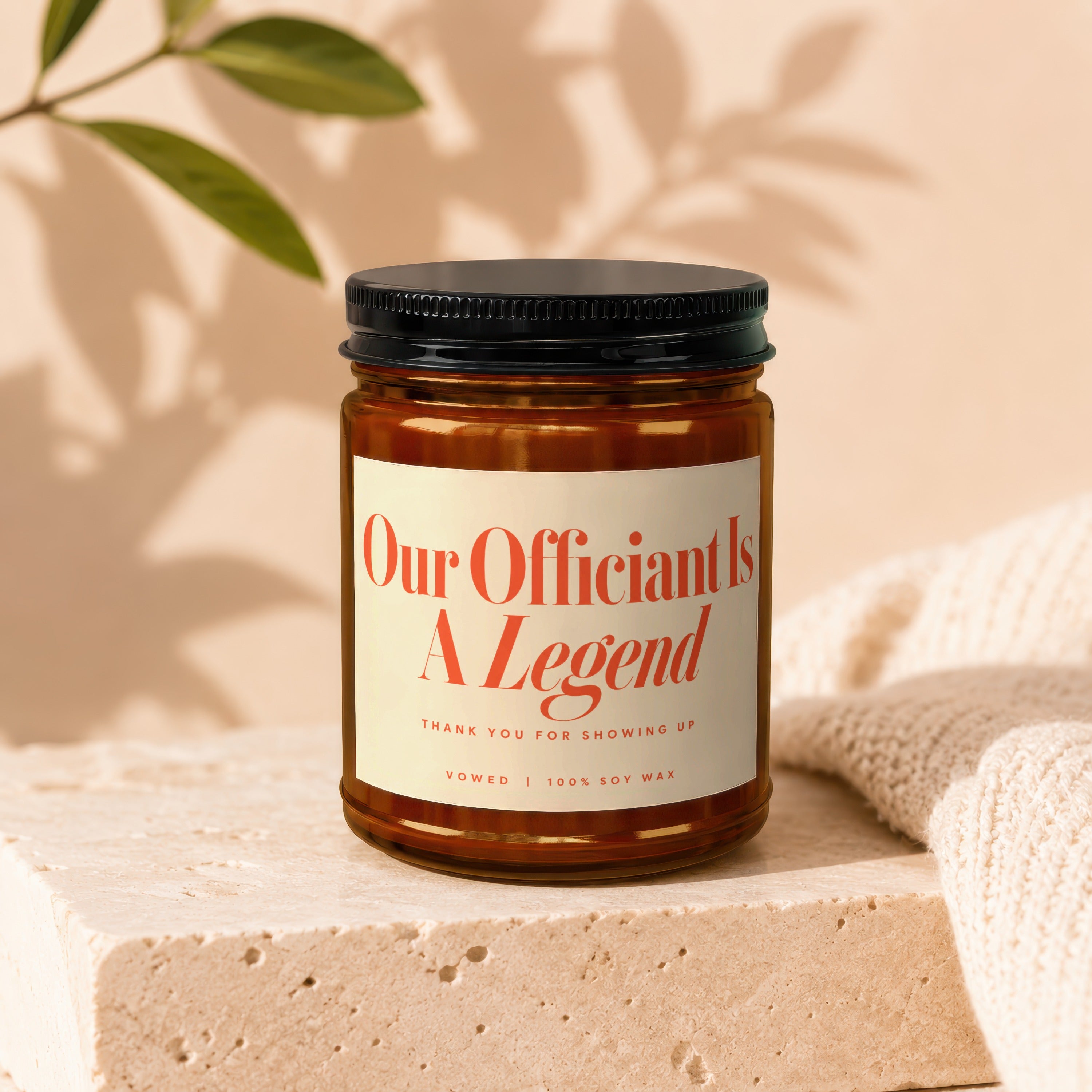 Amber jar candle with black lid, "Our Officiant Is A Legend" text, 100% soy wax.
