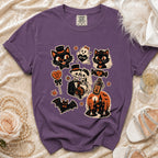 Purple t-shirt with Halloween icons: cats, ghost, skeletons, bat, haunted house, and candy.