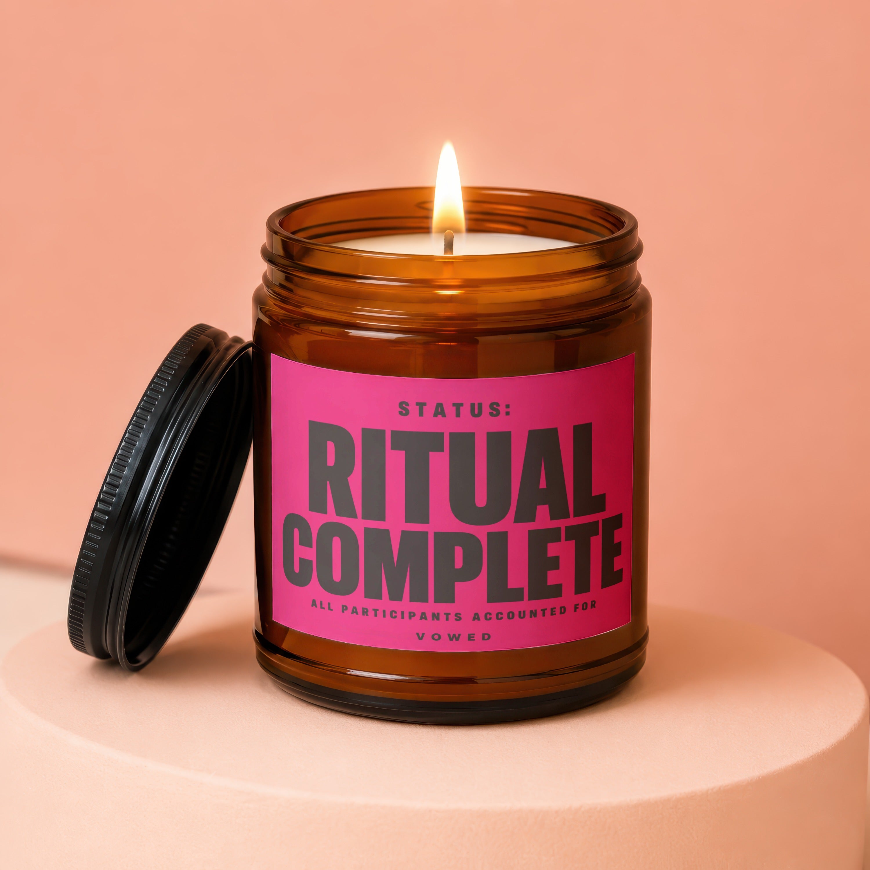 Amber jar candle burning with "Status: RITUAL COMPLETE" large on a pink label.