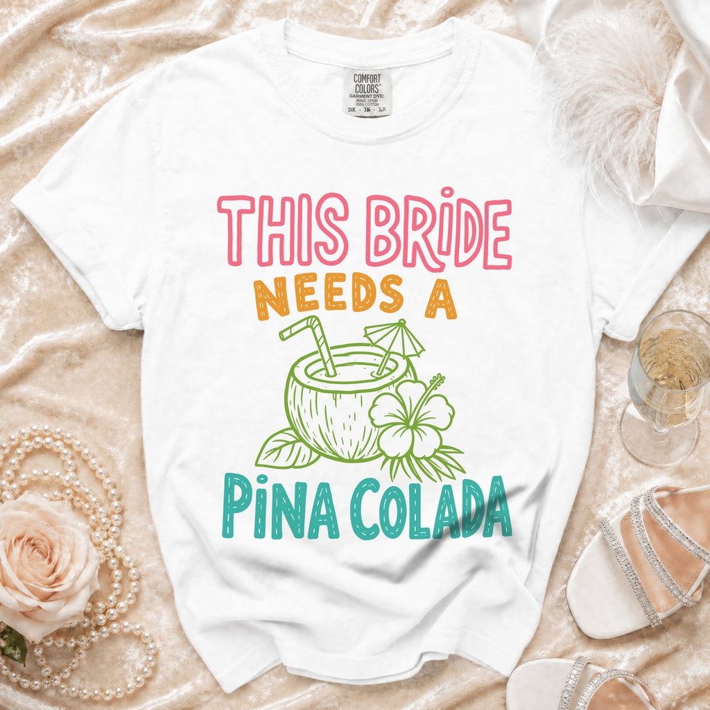 White t-shirt with "THIS BRIDE NEEDS A PINA COLADA" text and coconut graphic.
