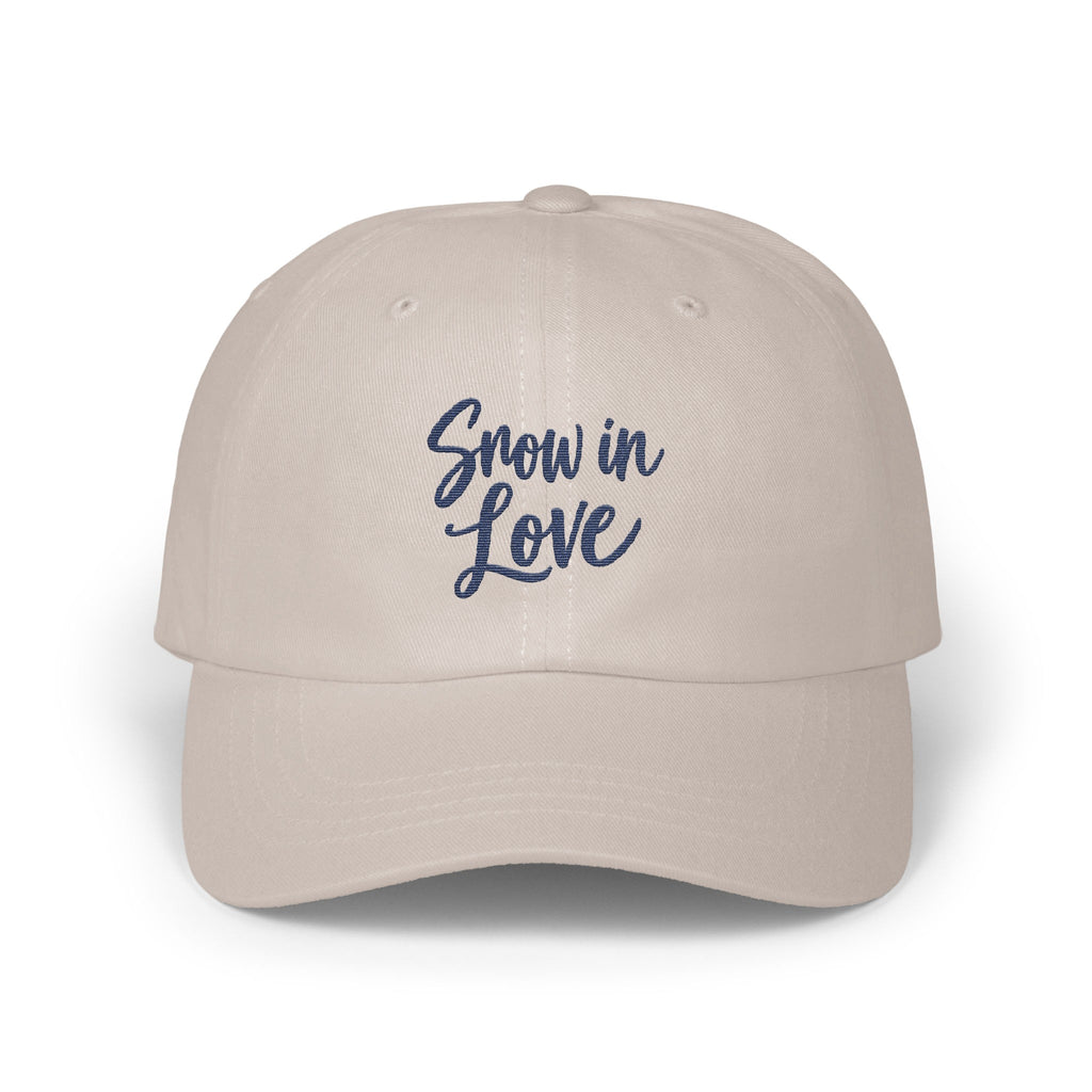 A light beige baseball cap with the blue embroidered text Snow in Love centered on the front panels.