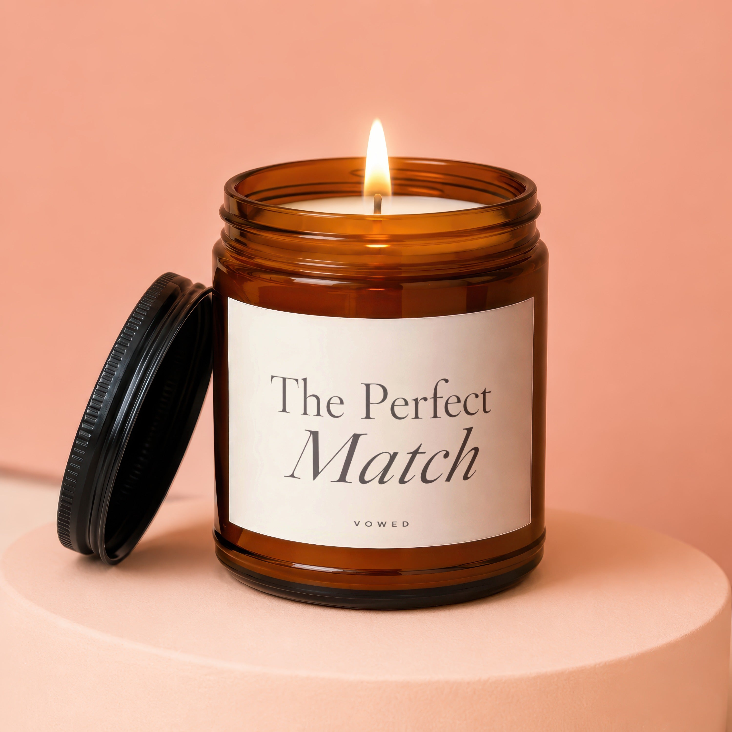 Amber glass candle with lit wick and lid. Label reads "The Perfect Match".