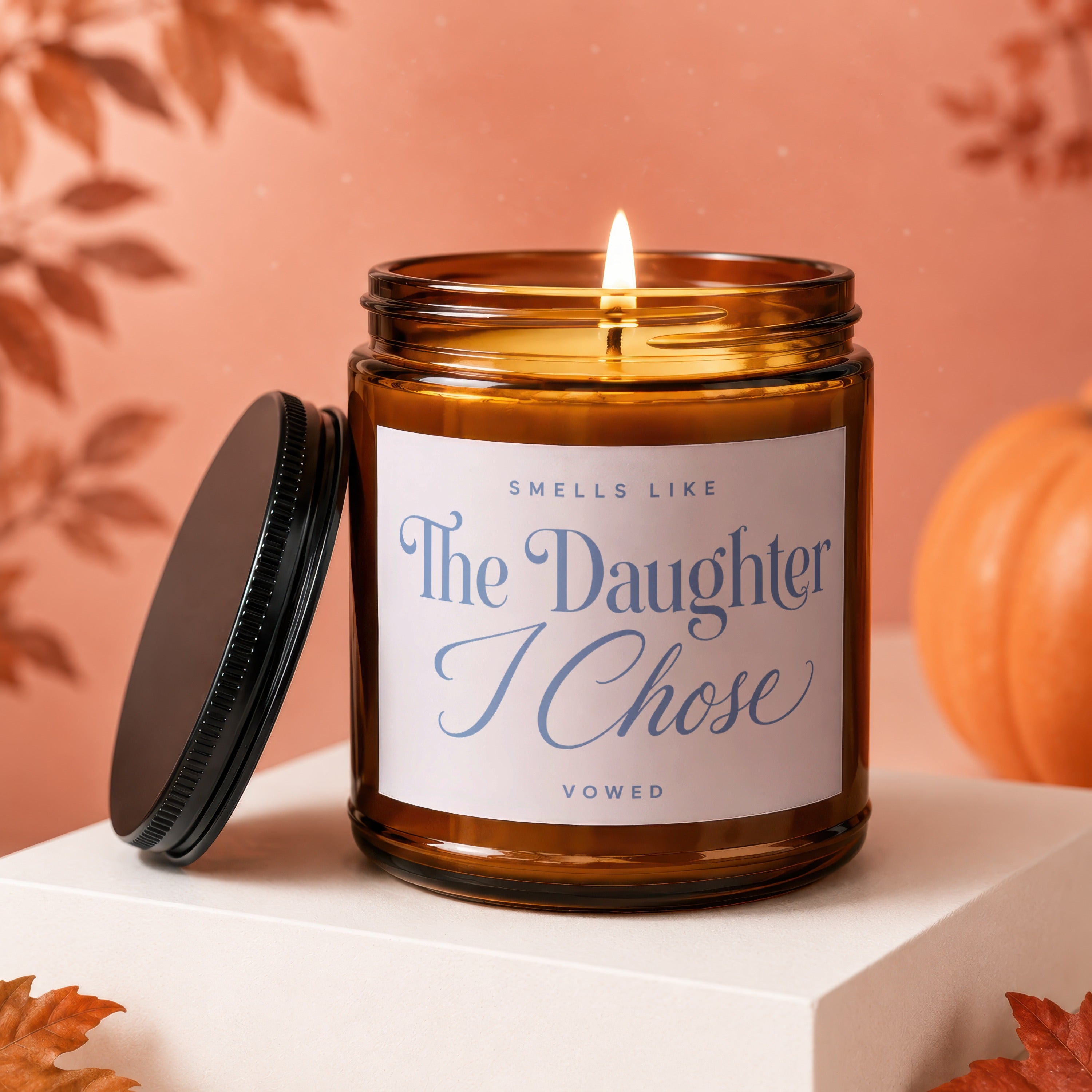 Amber jar candle with lit wick, label reads "Smells Like The Daughter I Chose Vowed".