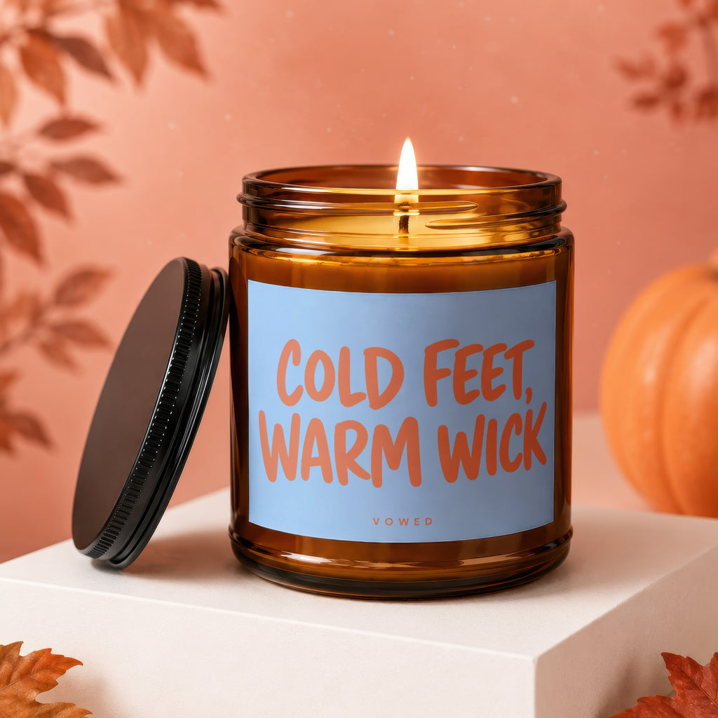 Amber jar candle with lit wick, reading "COLD FEET, WARM WICK" and "VOWED"