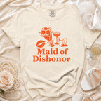 Cream t-shirt with orange floral, lip, and champagne glass graphic and text "Maid of Dishonor".