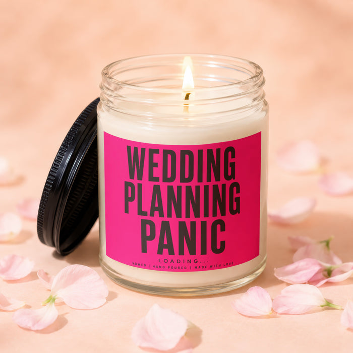Lit candle in a glass jar with a pink label reading "Wedding Planning Panic".