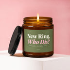 Amber glass candle with lit wick, lid ajar, reads "New Ring, Who Dis?".
