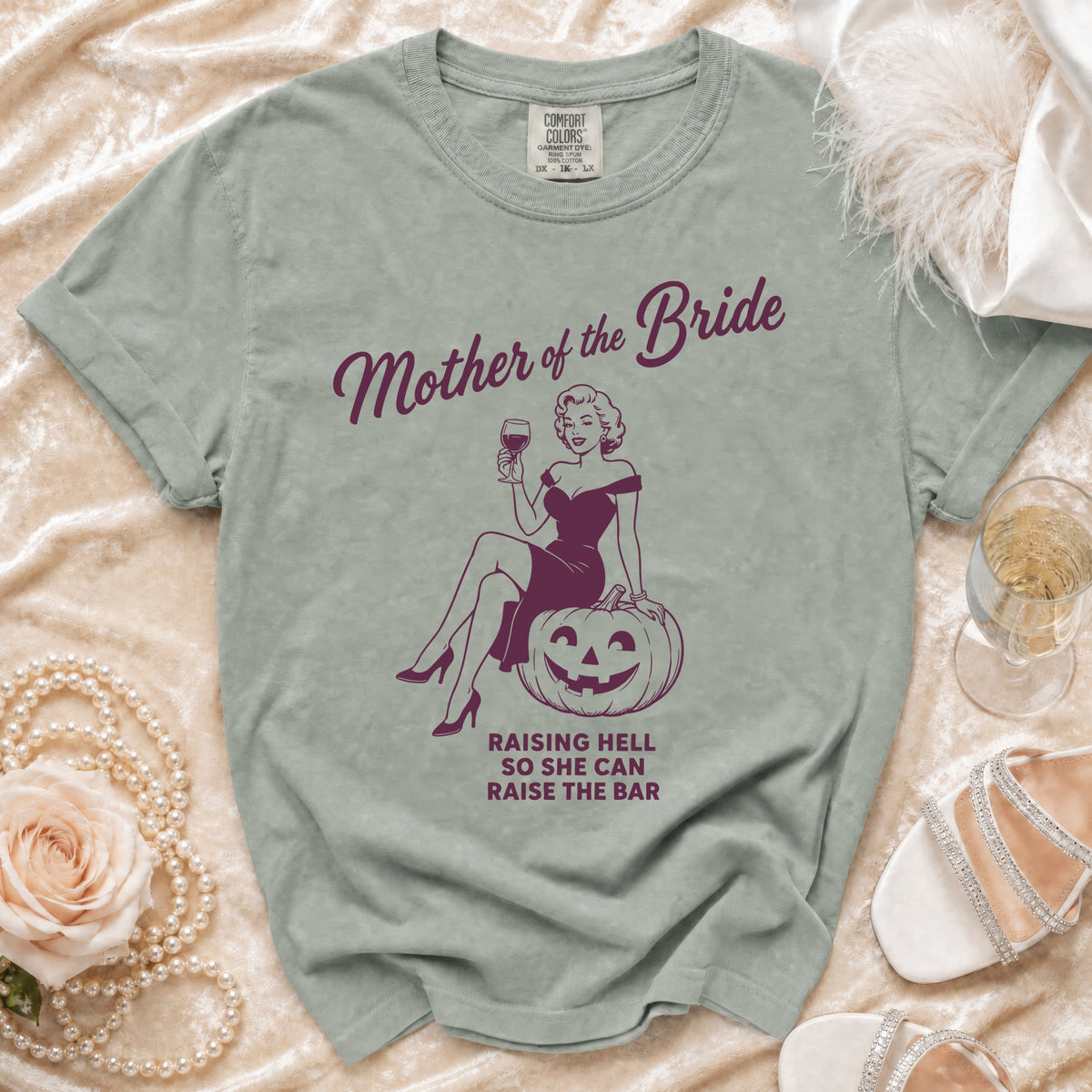 "Mother of the Bride" shirt with a pin-up graphic and text "Raising Hell So She Can Raise the Bar".