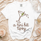 White t-shirt with martini glass graphic and "a tini bit tipsy" text.