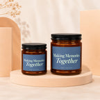 Two amber glass candles with black lids and blue labels reading "Making Memories Together".