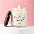 Lit candle in a glass jar with a black lid, reading "The Perfect Match"