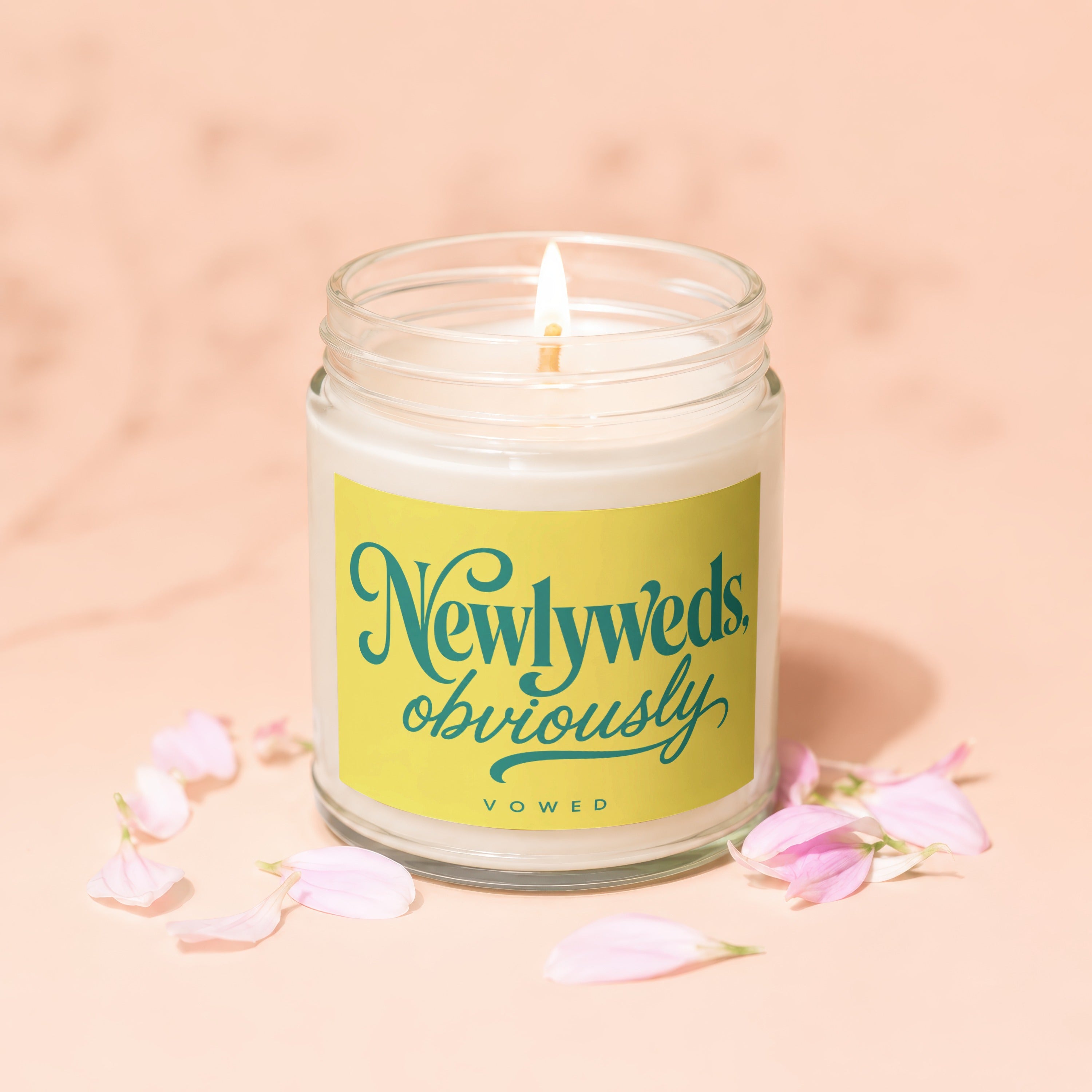 Scented candle with "Newlyweds obviously" text on yellow label and pink petals.